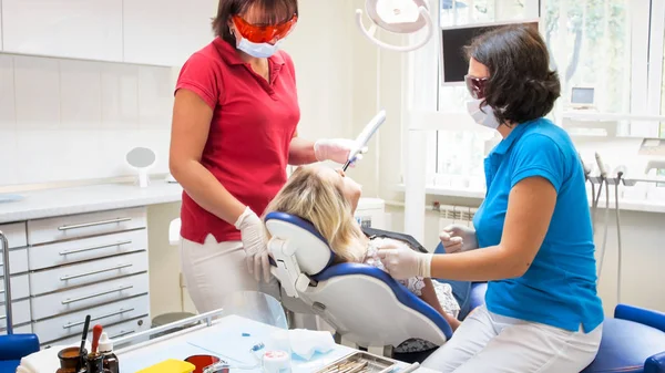 Assistente de dentista usando lâmpada de cura dentária uv em pacientes dentes — Fotografia de Stock