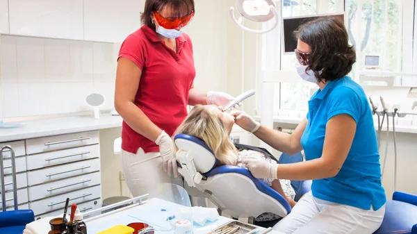 Dentista che cura i pazienti denti con lampada UV per indurimento dentale — Foto Stock
