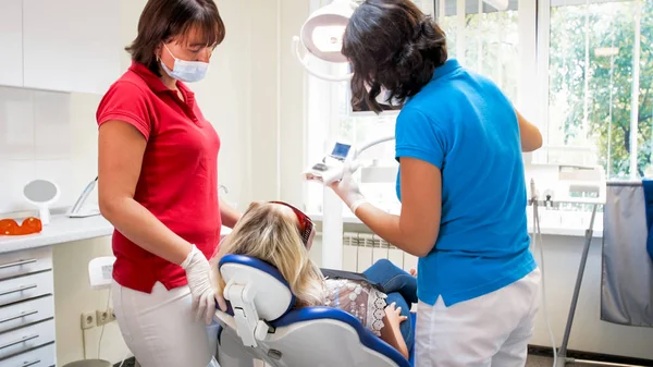 Dentista feminino e assistente ajustando dentes especiais branqueamento lâmpada ultravioleta — Fotografia de Stock