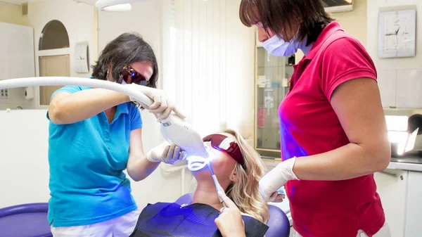Dentista e assistente em óculos laranja protetores durante o procedimento de clareamento dos dentes com luz UV — Fotografia de Stock