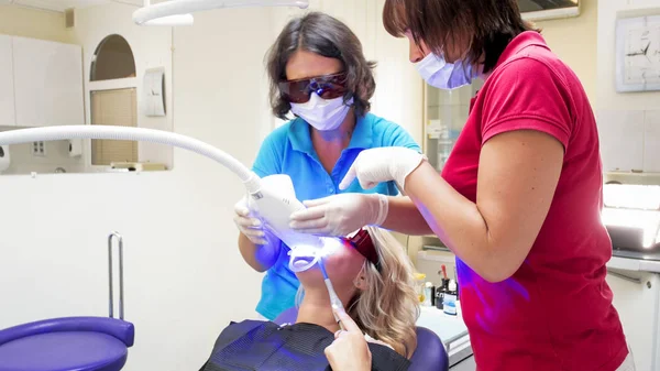 Dentista feminino usando lâmpada de luz ultravioleta especial para o procedimento de clareamento dos dentes — Fotografia de Stock