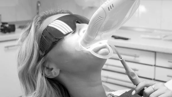 Чорно-біле зображення молодої жінки в захисних рукавичках під час процедури відбілювання зубів — стокове фото