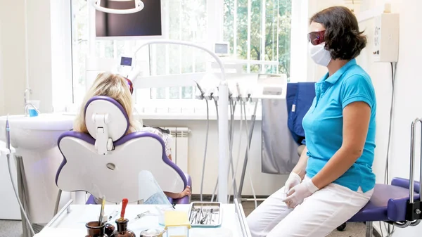 Dentista olhando para a jovem mulher sentada na cadeira do dentista durante o procedimento de bruxaria dos dentes — Fotografia de Stock