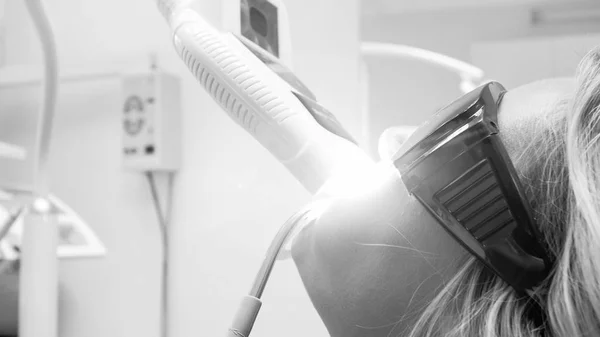 Black and white image of young woman sitting in dentist office during teeth whitening — Stock Photo, Image