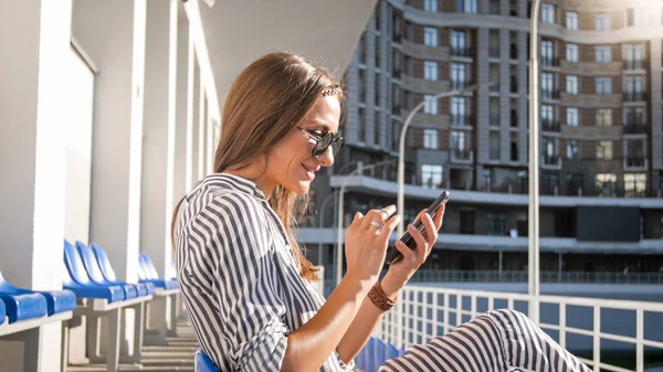 Closeup portrait of stylish young woman sitting on bench on street and using smartphone — Stock Photo, Image