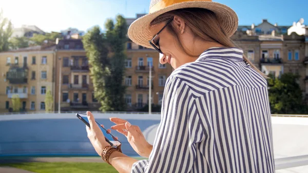 Retrato de mulher bonita e elegante em chapéu usando telefone celular na rua no dia ensolarado de verão — Fotografia de Stock