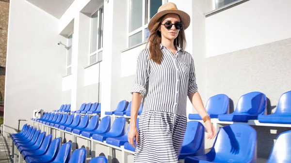 Hermosa mujer elegante en sombrero de verano caminando entre filas vacías de asientos — Foto de Stock