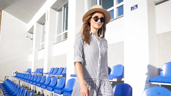Jeune femme élégante en lunettes de soleil et chapeau marchant sur le stade vide — Photo