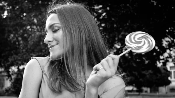 Black and white image of beautiful young woman posing with lollipop on street — Stock Photo, Image