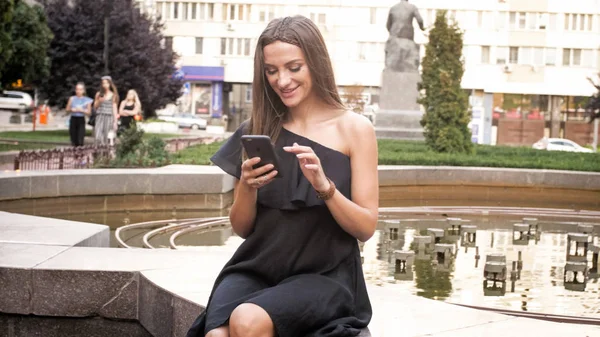 Ritratto di bella donna sorridente seduta alla fontana e utilizzando il telefono cellulare — Foto Stock