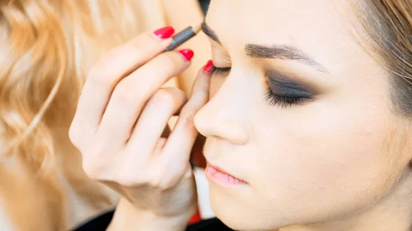 Closeup image of models face sitting in beauty salon hwile makeup artist applies makeup — Stock Photo, Image