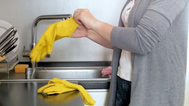 Imágenes de primer plano de 4k de la joven ama de casa parada en la cocina y poniéndose guantes de goma amarillos — Vídeo de stock