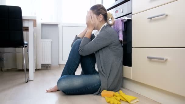 4k кадри засмученої і втомленої домогосподарки, що плаче на підлозі на кухні — стокове відео