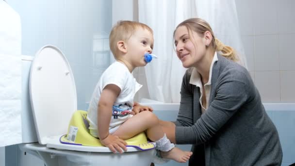 4 k beelden van jonge moeder praten en zingen terwijl het onderwijzen van haar zoontje gebruik van toilet — Stockvideo