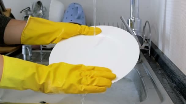 Closeup αργή κίνηση μήκος σε πόδηα της νοικοκυράς στα κίτρινα λαστιχένια γάντια πλύσιμο των πιάτων στο νεροχύτη της κουζίνας — Αρχείο Βίντεο