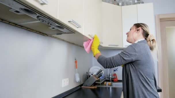 Vídeo em câmera lenta de uma jovem dona de casa feliz ouvindo música com fones de ouvido enquanto lava e limpa a cozinha — Vídeo de Stock