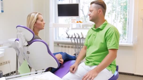 4 k πλάνα του όμορφος αρσενικό οδοντίατρος, μιλάμε για τον ασθενή γυναίκα κάθεται στην οδοντιατρική καρέκλα — Αρχείο Βίντεο