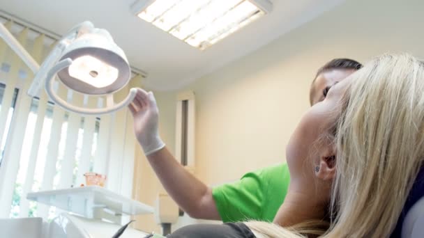 Imágenes de primer plano de 4k del dentista ajustando la lámpara y mirando al paciente sentado en la silla — Vídeo de stock