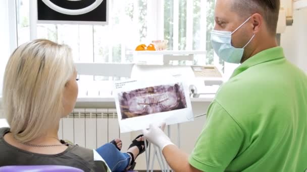 4k footage of dentist explaining teeth treatment to his patient on x-ray image of mouth — Stock Video