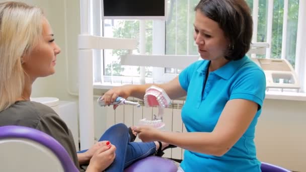 Kadın diş hekimi hastaya nasıl elektrik fırça ile dişleri temizlemek için öğretim 4 k görüntüleri — Stok video