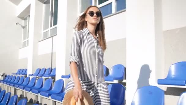 Vidéo 4k de souriante femme élégante marchant sur le stade vide à la journée ensoleillée brillante — Video