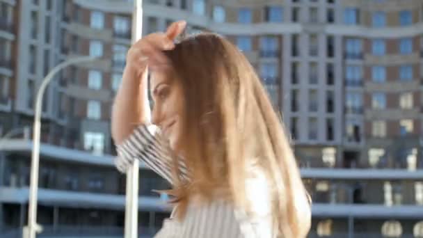 Vidéo 4k de belle jeune femme marchant dans la rue à la journée venteuse et regardant la caméra — Video