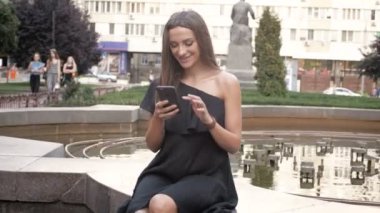 Parkta oturan ve smartphone kullanarak siyah elbiseli güzel genç kadın
