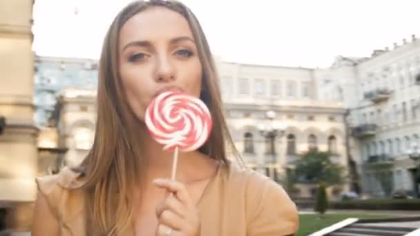 Primer plano 4k metraje de feliz joven mujer caminando en la calle y lamiendo piruleta — Vídeo de stock