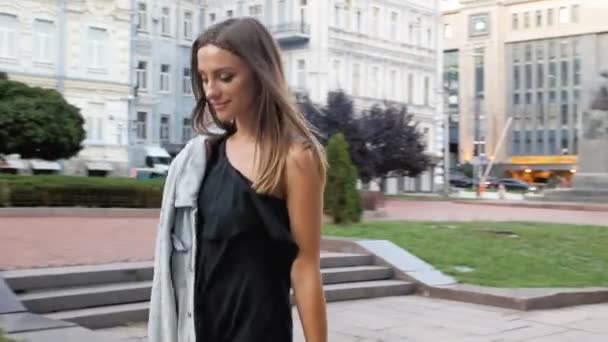 4k imagens de elegante jovem mulher em vestido preto andando no parque — Vídeo de Stock