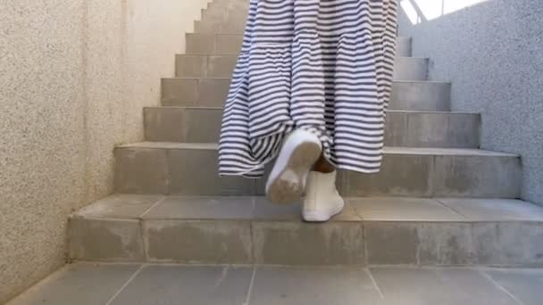 Images de vue arrière au ralenti d'une femme élégante en robe longue et baskets montant les escaliers dans la rue — Video