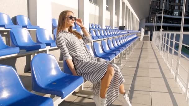 Slow motion beelden van stijlvolle jongedame ontspannen op leeg stadion op warme zonnige dag — Stockvideo