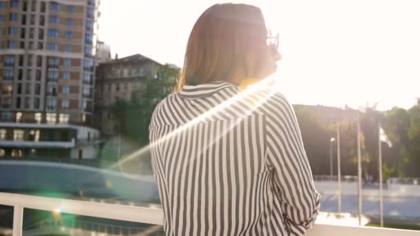 Slow motion video of stylish young woman standing on street and looking at sunset over city — Stock Video