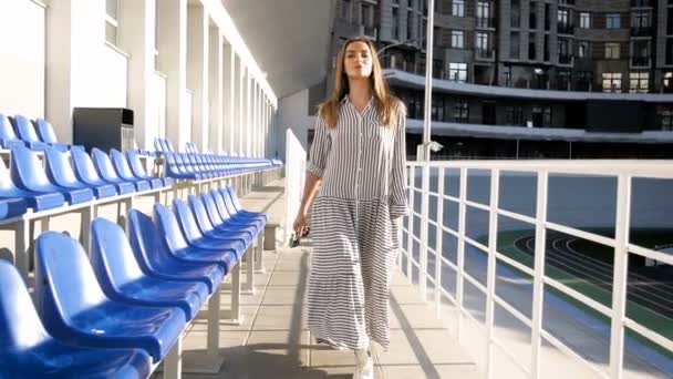 Zpomalené video krásná mladá žena chůze mezi řadami sedadel na prázdný stadion — Stock video