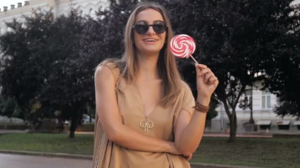 Vídeo en cámara lenta de la feliz mujer sonriente posando en el parque con gran piruleta — Vídeos de Stock