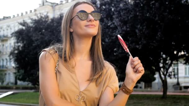 Slow motion footage of beautiful smiling woman with lollipop standing on street — Stock Video