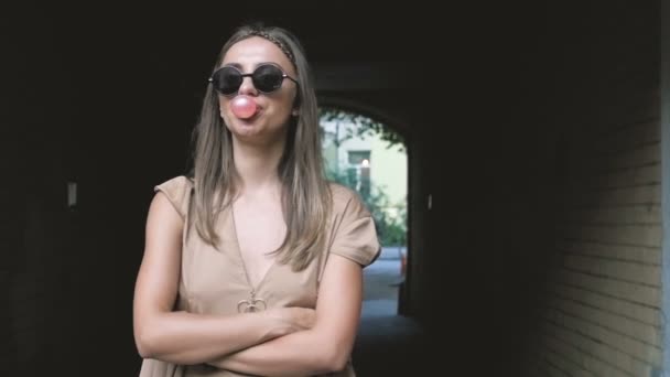 Imágenes en cámara lenta de la joven mujer con estilo en gafas de sol que soplan burbujas de goma de mascar — Vídeos de Stock