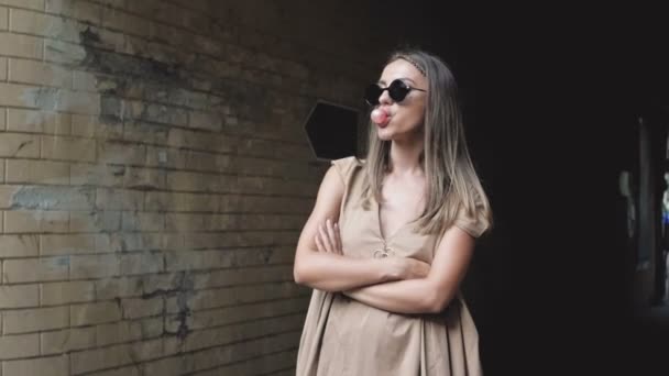 Повільне відео руху стильної молодої жінки, що стоїть на вулиці і жує жувальну гумку — стокове відео