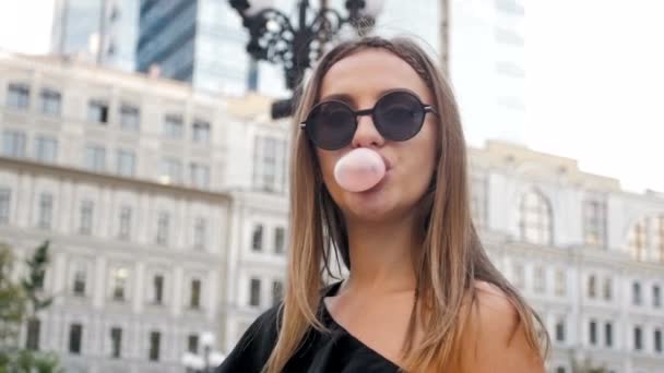 Βίντεο αργής κίνησης closeup νεαρή γυναίκα σε γυαλιά ηλίου ψάχνει στην κάμερα και Blow τσίχλα — Αρχείο Βίντεο