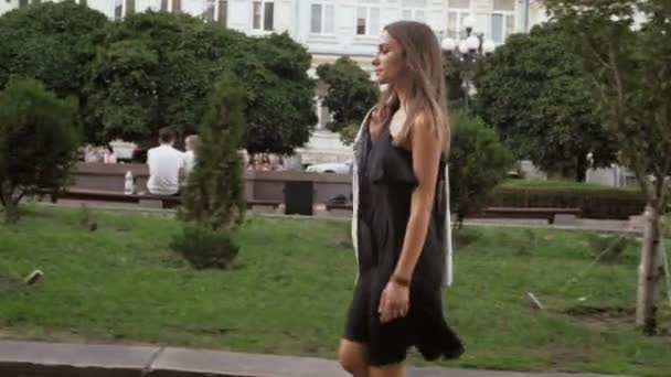 Vídeo em câmera lenta de jovem elegante em vestido preto curto andando no parque — Vídeo de Stock