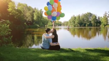 Genç çift rahatlatıcı nehrin yanında öpüşme ve büyük renkli balonlar demet tutan slow motion video