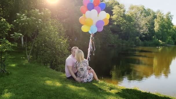 Відео повільного руху молодої пари з кульками, що обіймаються і цілуються біля озера — стокове відео