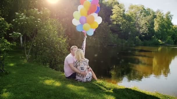 Vídeo en cámara lenta de una hermosa pareja joven enamorada sentada junto al lago y besándose — Vídeo de stock