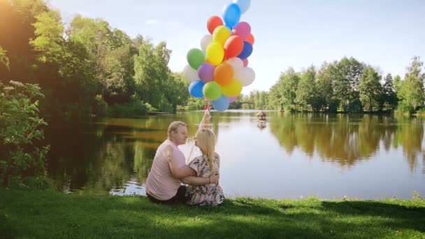 Vídeo en cámara lenta de una hermosa pareja romántica enamorada sosteniendo un gran manojo de globos y abrazándose al lago — Vídeo de stock