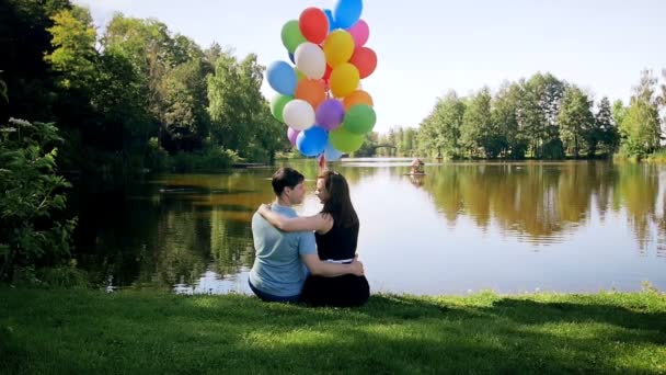 Imágenes en cámara lenta de hermosa pareja joven relajándose junto al lago y besándose — Vídeo de stock