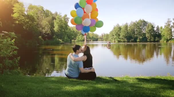 Slow motion video van jonge kussend koppel ontspannen door de rivier en het bedrijf grote bos van kleurrijke ballonnen — Stockvideo