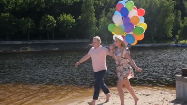 Zeitlupenvideo von glücklichem jungen Paar, das mit einem großen Haufen Luftballons rennt — Stockvideo