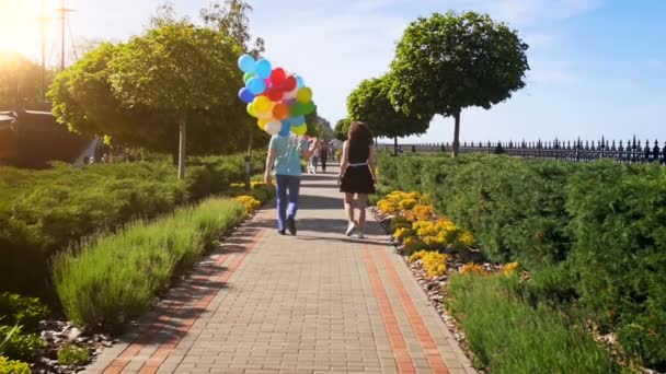 Vídeo em câmera lenta de jovem casal com um monte de balões coloridos andando no parque — Vídeo de Stock