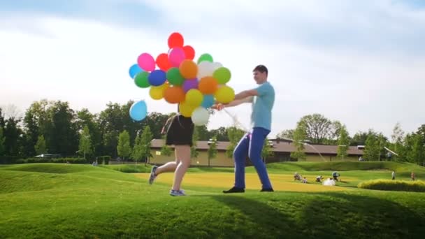 Vídeo em câmera lenta de feliz rindo jovem casal segurando balões coloridos e dançando no parque — Vídeo de Stock