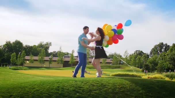 公園でハグ色とりどりの風船の束を持つ幸せな若いカップルのスロー モーション ビデオ — ストック動画