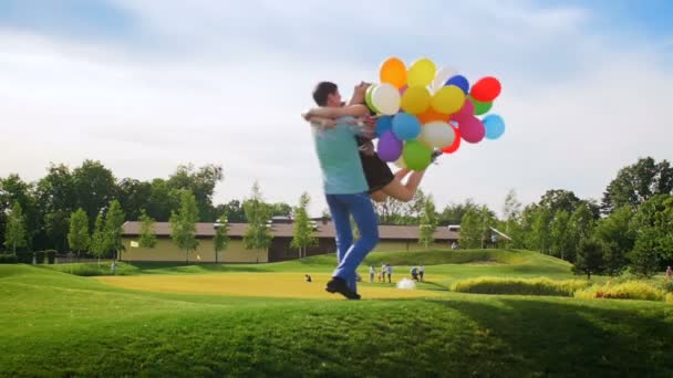 Vídeo en cámara lenta de feliz alegre pareja joven sosteniendo globos de colores y divertirse en el parque — Vídeos de Stock